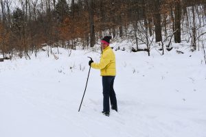 The author, wearing a bright yello down jacket, jeans, and black mittens, pauses while cross country skiing.